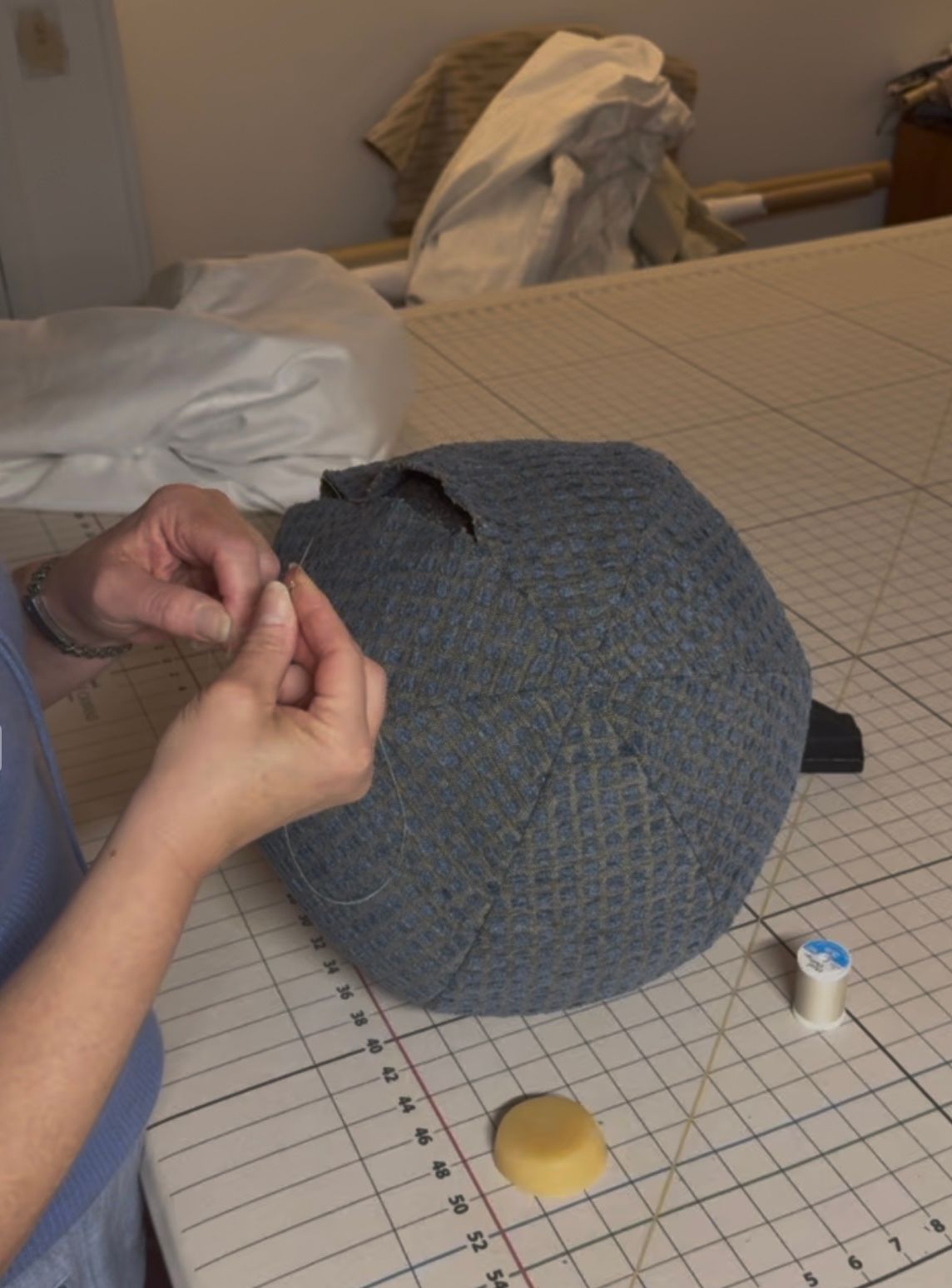 Amy's hands stitching a check-fabric ottoman on the workroom's gridded cutting table