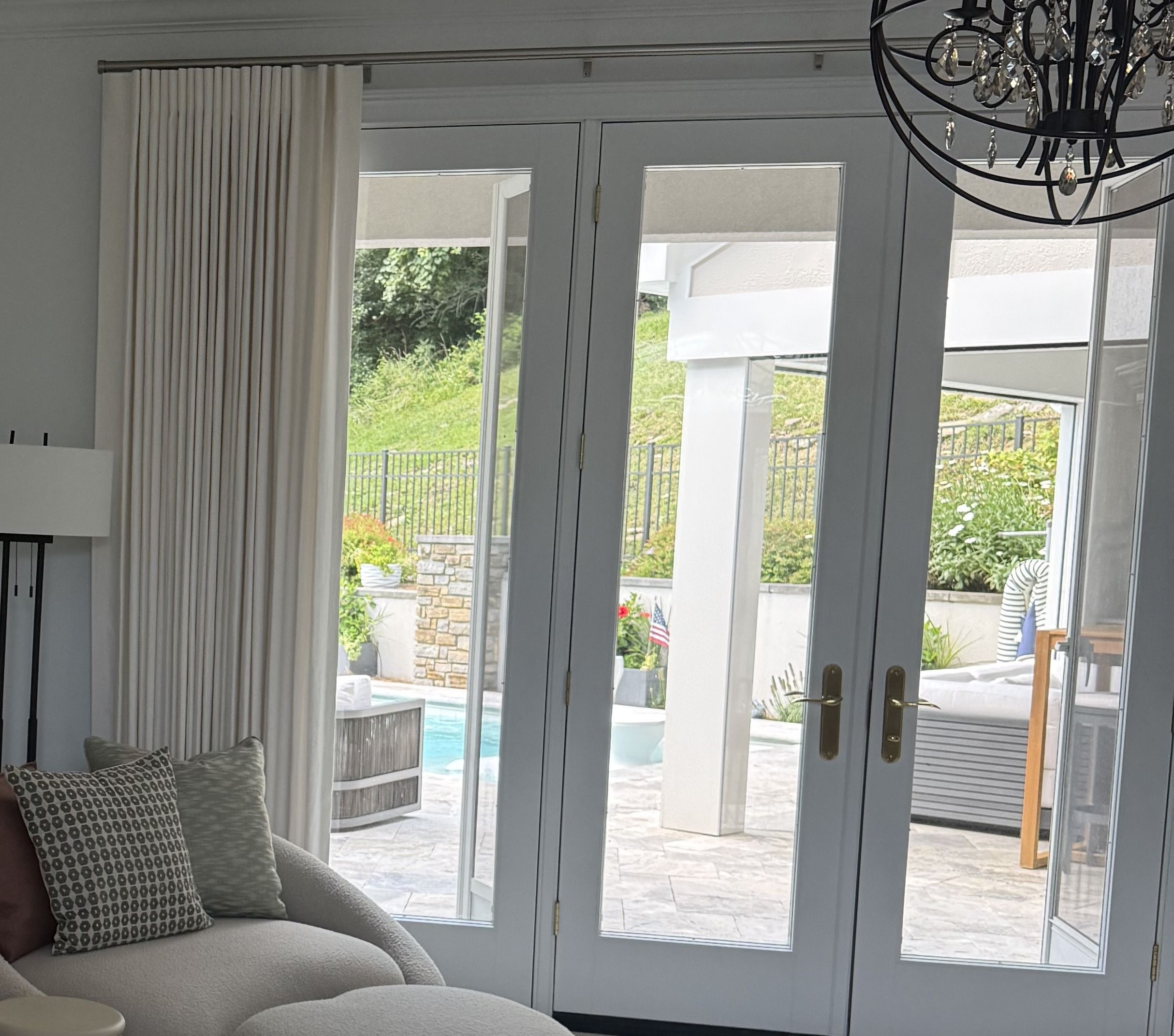 Banded roman shade and pleated drapery framing French doors, with a crystal chandelier overhead
