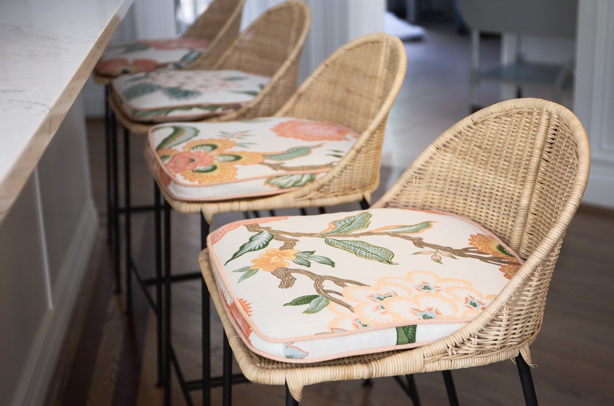Botanical-print seat cushions in peach and sage on cream, made for a row of rattan counter stools at a kitchen island