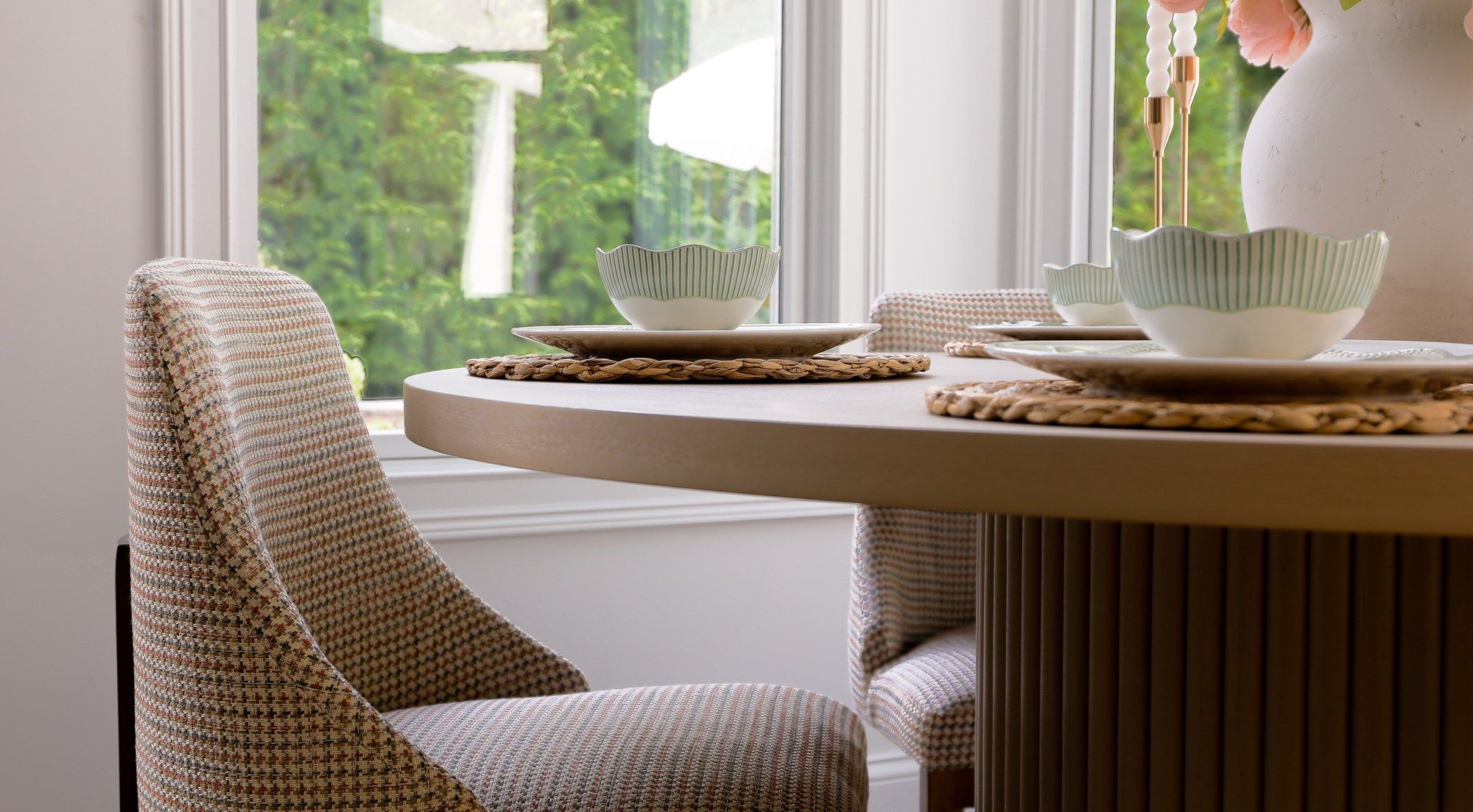 A dining chair reupholstered in a rust-and-taupe houndstooth fabric, at a round table in a breakfast room