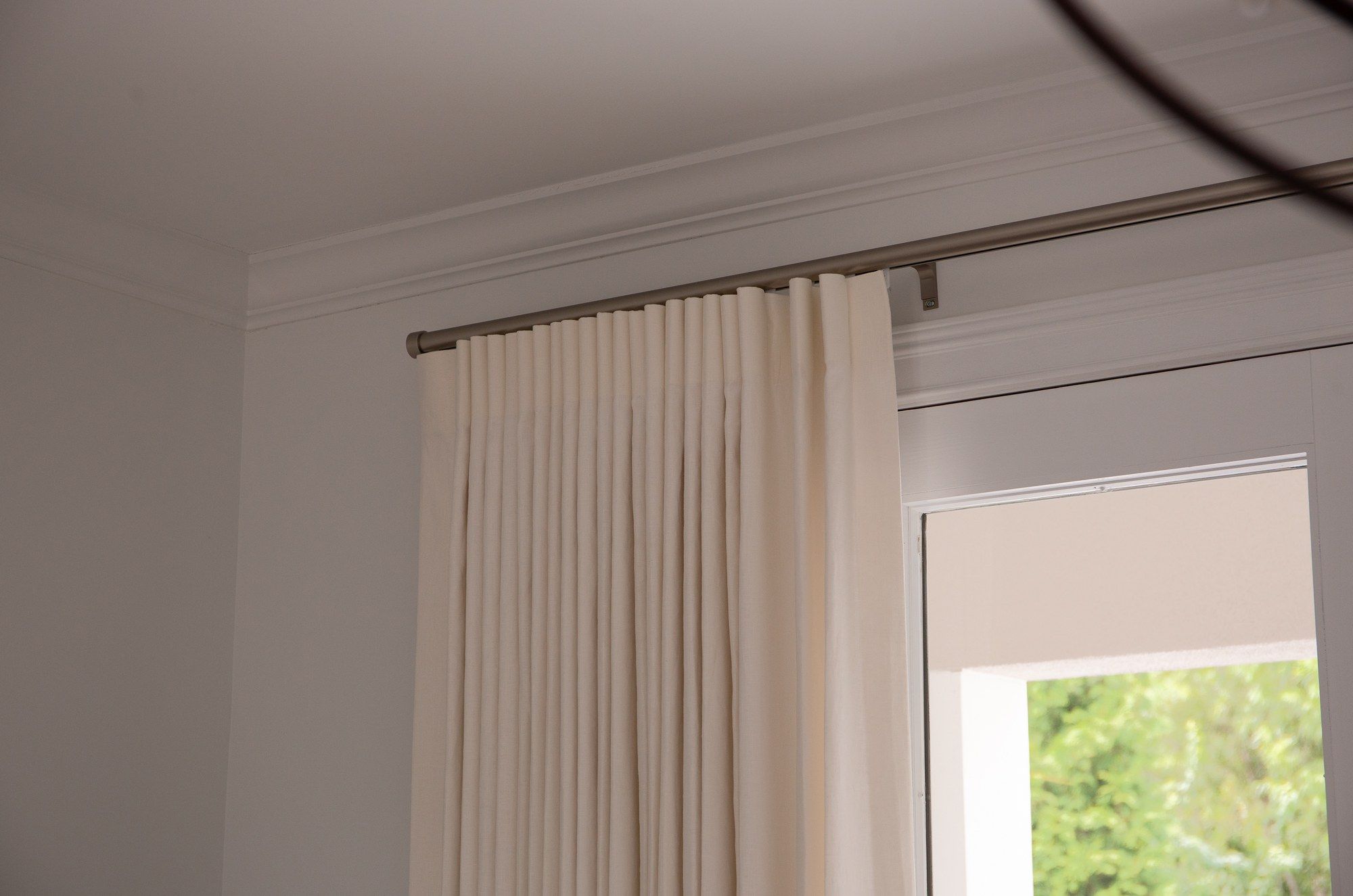 Ivory pinch-pleat drapery hanging full length from a brushed-nickel rod to the floor, beneath crown molding