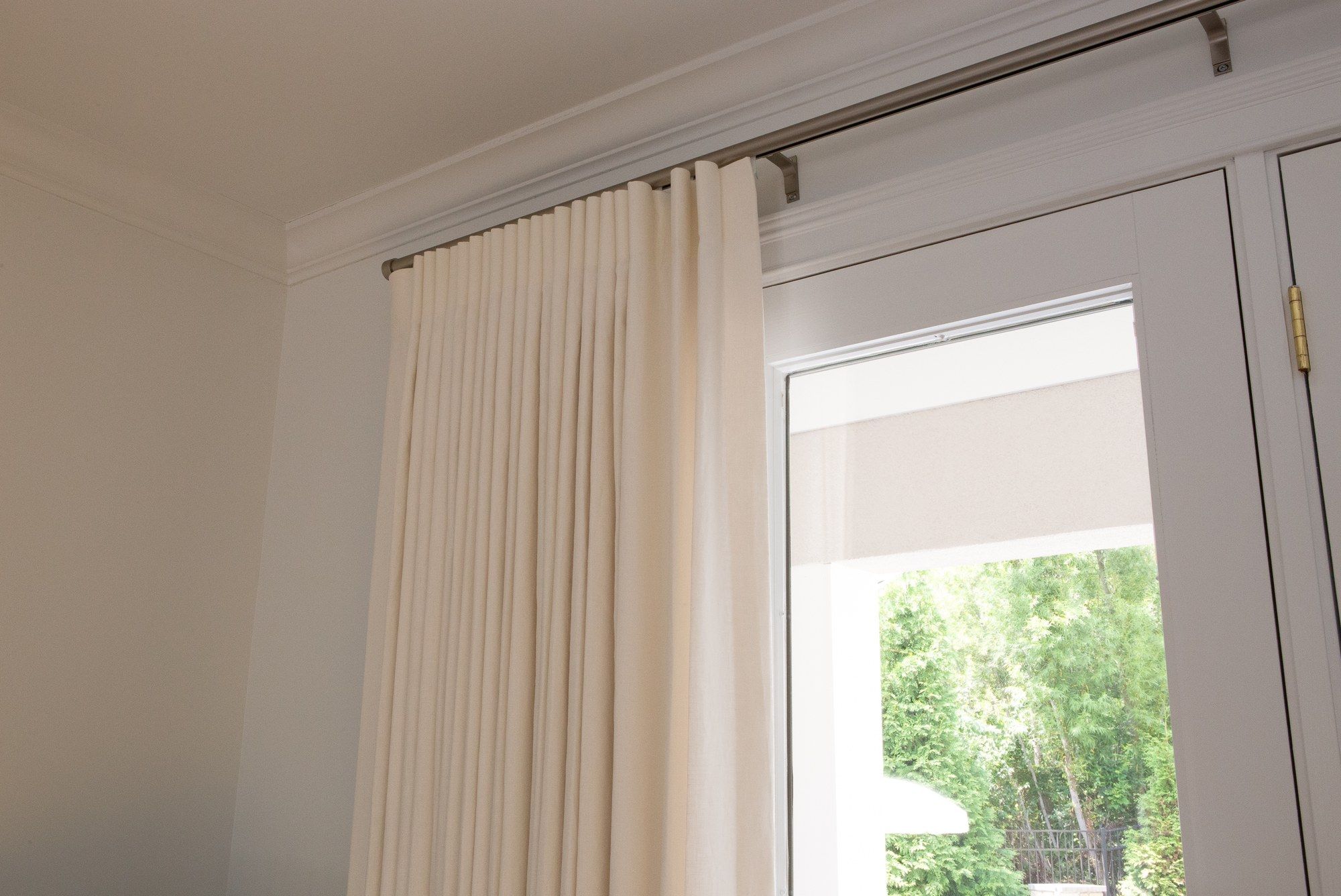 Detail of ivory pinch-pleat drapery rings on a brushed-nickel rod, with crown molding above and the panel falling into a stacked pleat