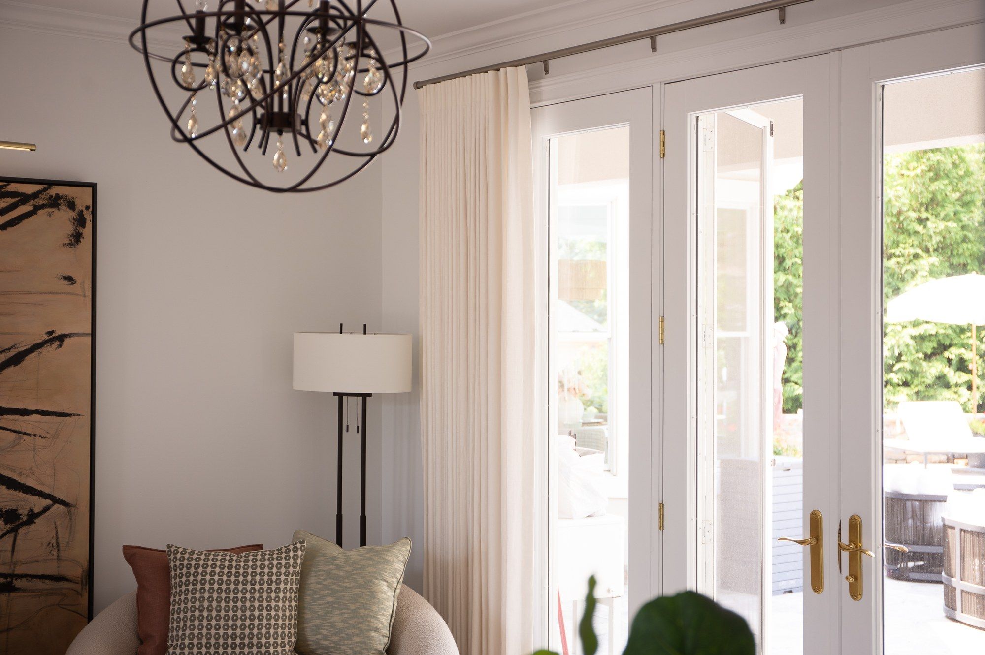 Ivory pinch-pleat drapery framing French doors in a living room, with a wire-orb chandelier and an abstract painting on the near wall