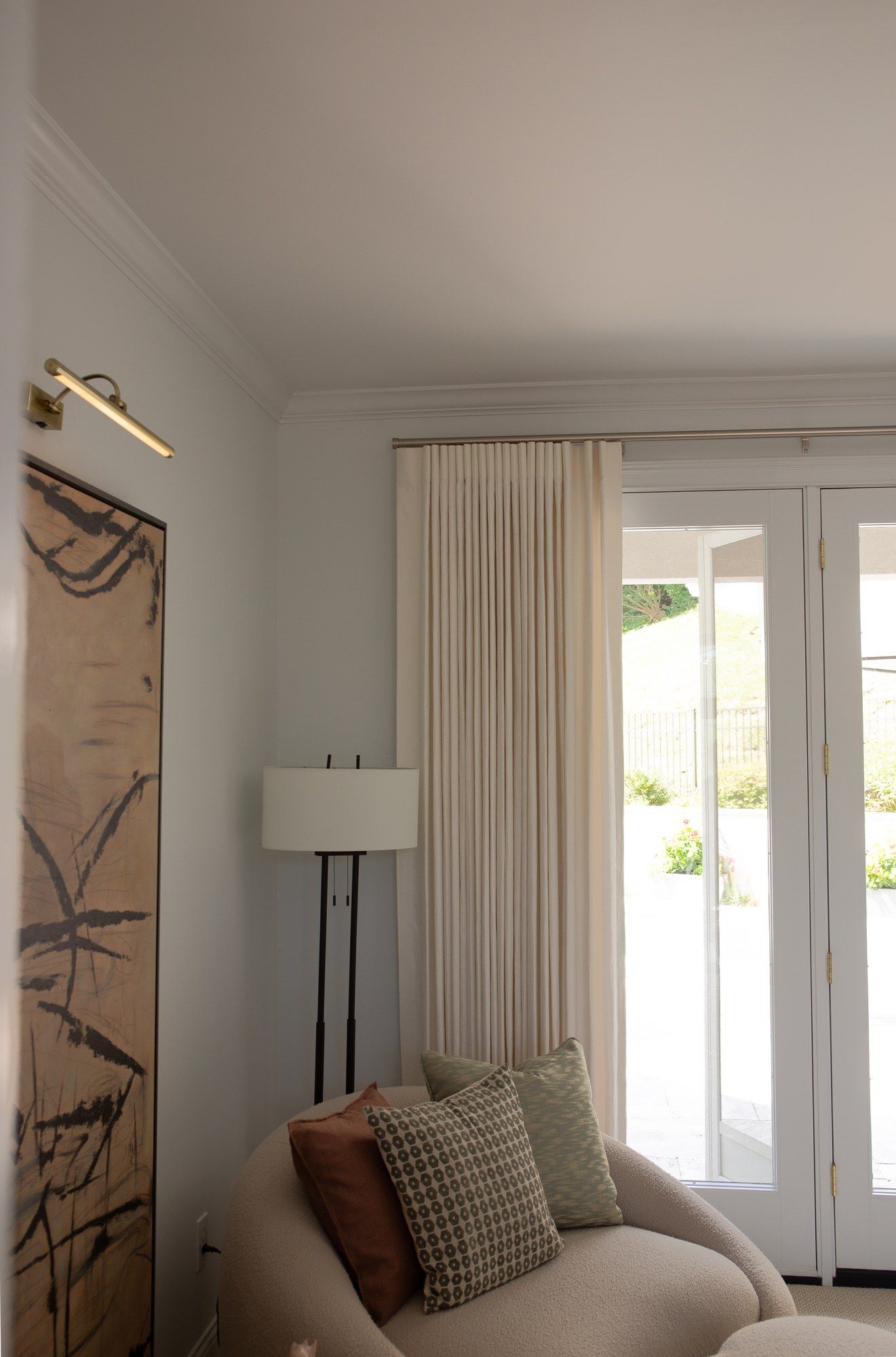 Ivory pinch-pleat drapery beside French doors in a reading nook, with a floor lamp and a framed abstract painting